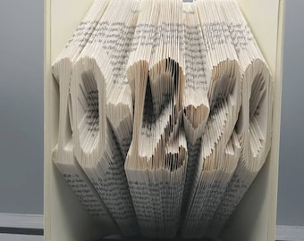 May include: A book folded into the shape of the word "LOVE" in a white, cream, and beige color scheme. The book is open and the pages are folded to create the letters.