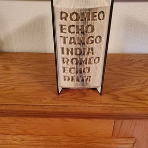 Puede incluir: Un libro negro con las palabras "ROMEO ECHO TANGO INDIA ROMEO ECHO DELTA" plegado en una escultura 3D.