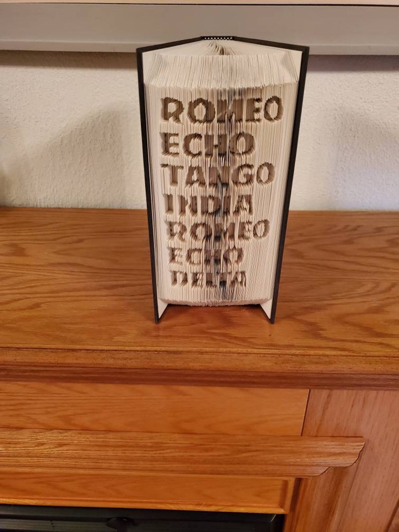 Puede incluir: Un libro negro con las palabras "ROMEO ECHO TANGO INDIA ROMEO ECHO DELTA" plegado en una escultura 3D.
