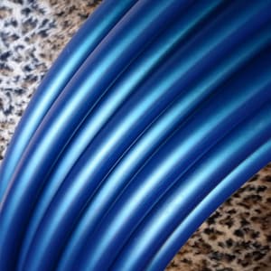 May include: Close-up of a set of blue hoop dance hoops. The hoops are made of a flexible material and have a metallic sheen.