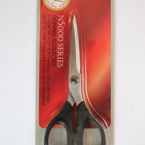 Może przedstawiać: Opakowanie nożyczek do szycia Kai N5000 Series, o długości 16,5 cm. Nożyczki mają czarne uchwyty i srebrne ostrza. Opakowanie jest czerwono-białe z tekstem "Feeling Good" i "Kai Original".