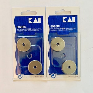 May include: Two packages of replacement blades for a 5028 wheel cutter. Each package contains two blades, made of tungsten steel and 28mm in diameter. The packages are blue and white with the brand name "ΚΑΙ" printed on them.