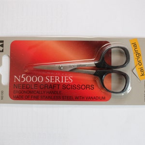 Może przedstawiać: Srebrne nożyczki do szycia z czarnymi uchwytami, zapakowane w przezroczysty blister z tworzywa sztucznego. Opakowanie jest czerwono-białe z tekstem "N5000 SERIES NEEDLE CRAFT SCISSORS ERGONOMICALLY HANDLE MADE OF FINE STAINLESS STEEL WITH VANADIUM" i "kai original".