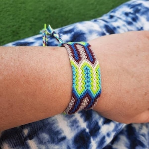 May include: A colourful friendship bracelet with a geometric pattern in shades of blue, green, white and brown.
