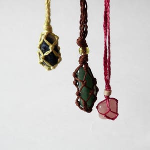 May include: Three handmade macrame necklaces with different colored stones. The necklaces feature a green stone, a blue stone, and a pink stone.