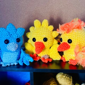 May include: Three crocheted stuffed animals: a blue bird, a yellow chick with orange beak, and a yellow chick with orange beak and orange fluffy feathers.