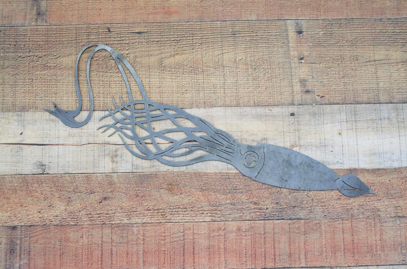 K&ouml;nnte beinhalten: Eine Wandskulptur aus Metall, die einen Tintenfisch mit langen Tentakeln darstellt. Die Skulptur ist silberfarben lackiert und auf einem Holzgrund montiert.