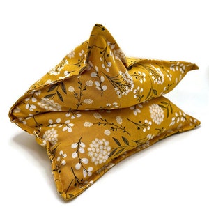 May include: Two mustard-yellow, star-shaped pillows with a floral pattern of white flowers and black stems. The pillows are stacked on top of each other, showcasing the detailed design and texture of the fabric.