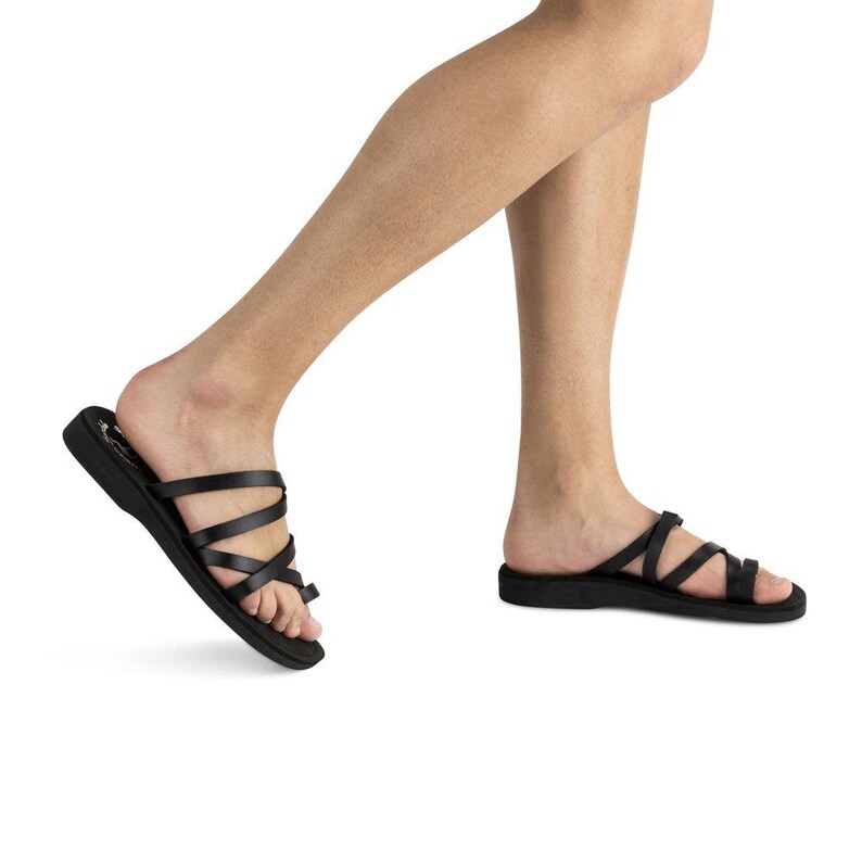 K&ouml;nnte beinhalten: Schwarze Ledersandalen mit mehreren Riemen, die sich &uuml;ber den Fu&szlig; kreuzen. Die Sandalen haben eine flache Sohle und ein bequemes Design.