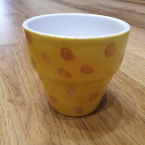 Può includere: Vaso di fiori in ceramica gialla con interno bianco e un motivo a macchie marrone-arancio. Il vaso è alto circa 10 cm e ha un diametro di 10 cm.