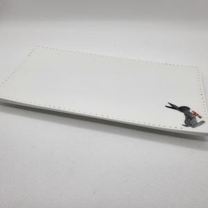 May include: A rectangular white ceramic serving platter with a decorative black rabbit holding a carrot in the corner. The edge of the platter is dotted with small gold-coloured accents.