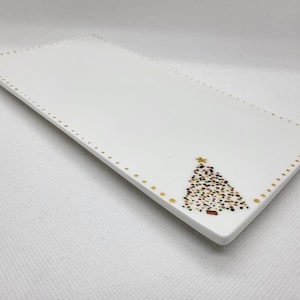 May include: A white rectangular ceramic serving platter with a gold dotted border. A Christmas tree design with colourful dots and a gold star is in the corner. A festive serving dish.