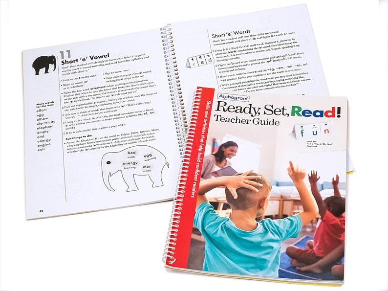 May include: A red and yellow teacher guide book titled "Ready, Set, Read!" with a picture of a teacher and students in a classroom. The book is part of the Alphagram program and features skills and activities to help build confident readers.
