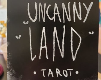 May include: A black card with white text that reads "The Uncanny Land Tarot".