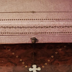 May include: A wooden box with a pink lid. The lid has a decorative design with a small metal knob. The box is made of dark wood with a light brown inlay.