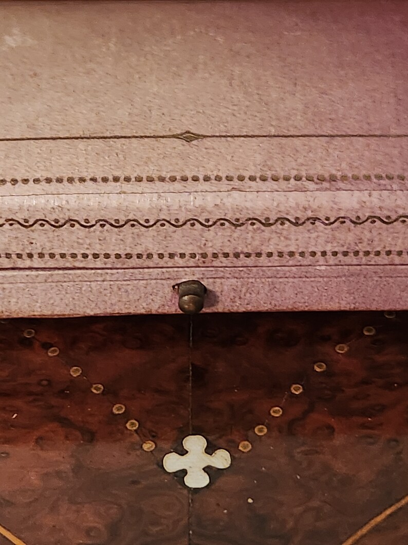 May include: A wooden box with a pink lid. The lid has a decorative design with a small metal knob. The box is made of dark wood with a light brown inlay.