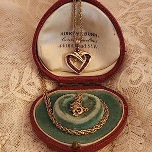 May include: A gold heart-shaped pendant necklace with red gemstones set in a twisted design. The necklace is in a red velvet heart-shaped box with the inscription "KIRKBY & BUNN, bourne jewellers, 44 Old Bond St., W."