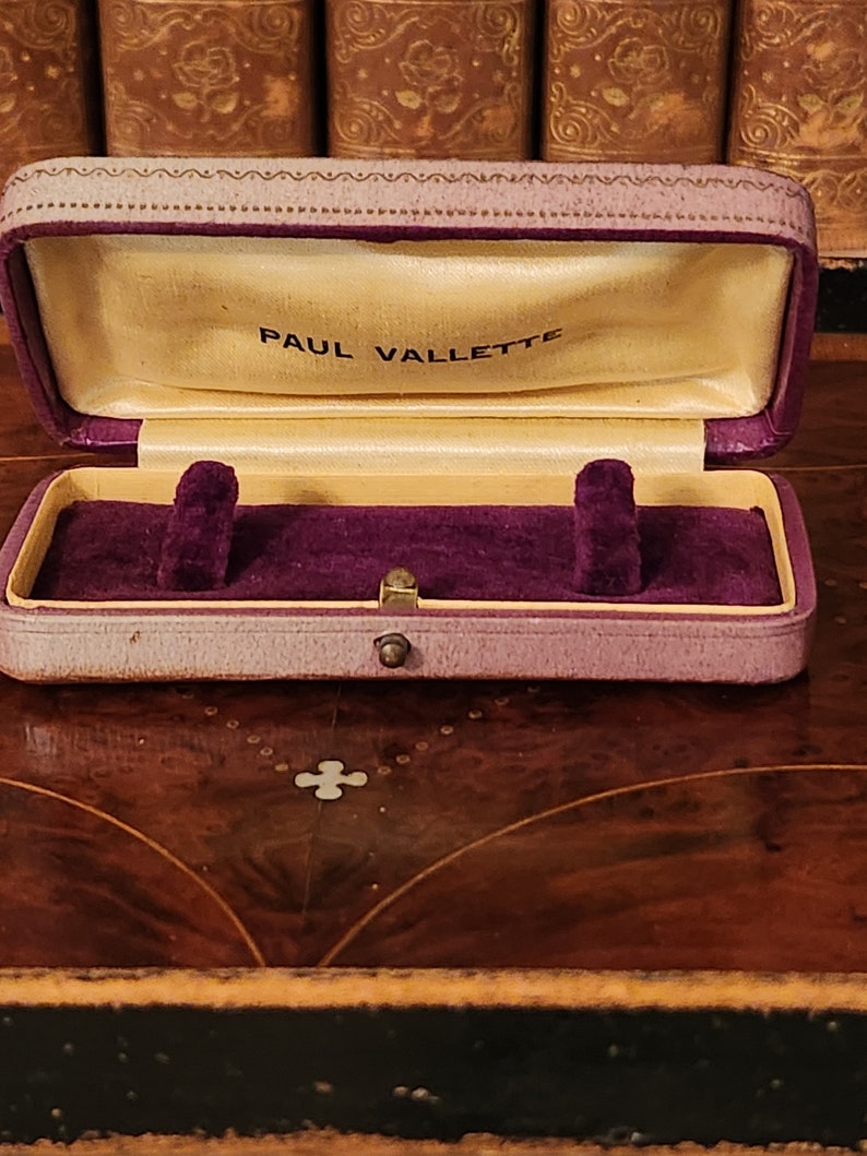 May include: A purple velvet-lined jewellery box with a gold clasp. The box is closed and has the words "PAUL VALLETTE" printed on the inside of the lid.