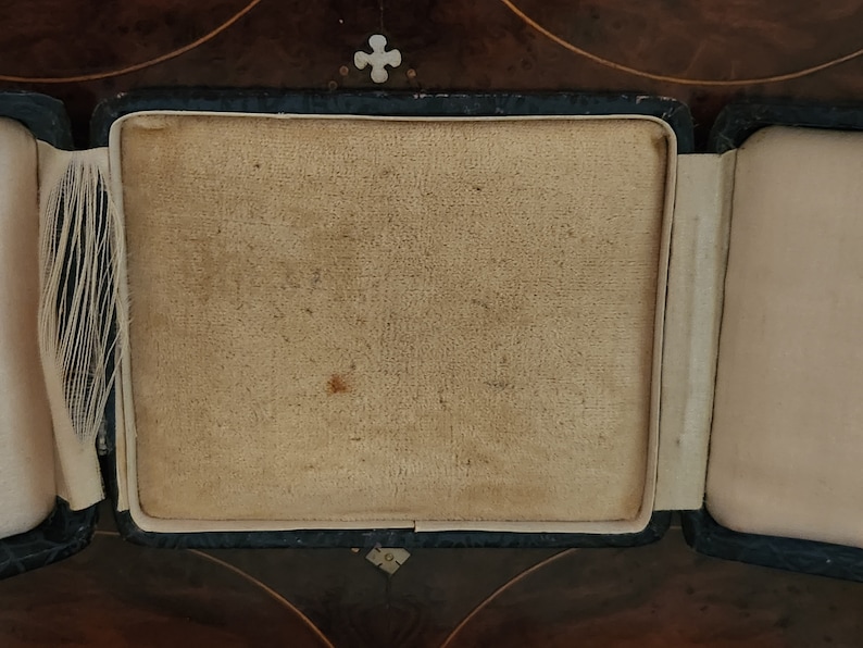 May include: A black velvet jewelry box with a beige interior. The box is open and the interior is empty.