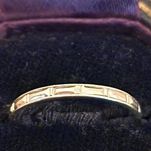 May include: A thin silver band with a decorative design of small rectangular shapes.