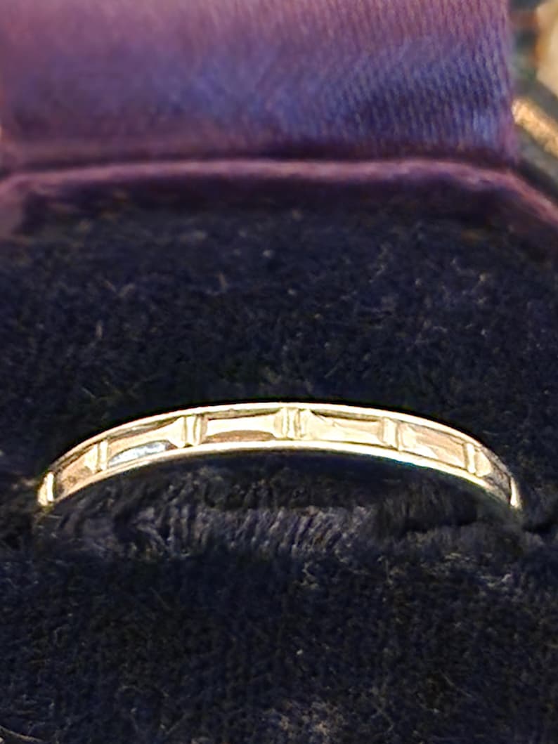 May include: A thin silver band with a decorative design of small rectangular shapes.