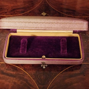May include: A small, purple velvet jewellery box with a gold trim and a decorative pattern on the lid. The box is open and the interior is lined with purple velvet.
