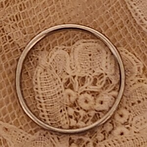 May include: A close-up of a silver ring on a white lace background.
