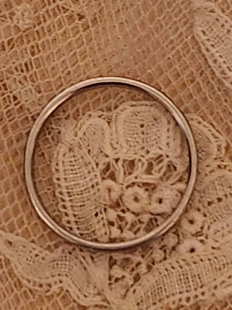 May include: A close-up of a silver ring on a white lace background.