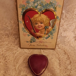 May include: Vintage Valentine's Day card featuring a cherub holding a bow and arrow, surrounded by blue flowers and hearts. The card reads "I love you as much as you can see, and I'll prove it, too, do you love me? To my Valentine."