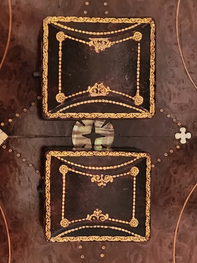 Puede incluir: Dos peque&ntilde;as cajas cuadradas de cuero marr&oacute;n con ribetes dorados y dise&ntilde;os ornamentados. Las cajas est&aacute;n sobre una superficie marr&oacute;n oscuro con un patr&oacute;n de peque&ntilde;os puntos blancos.