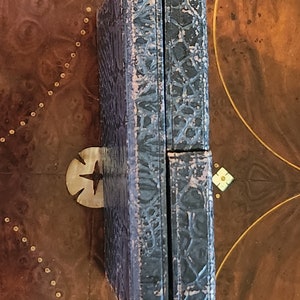 May include: A dark blue, rectangular box with a textured, patterned surface. The box is closed and has a hinge on one side.