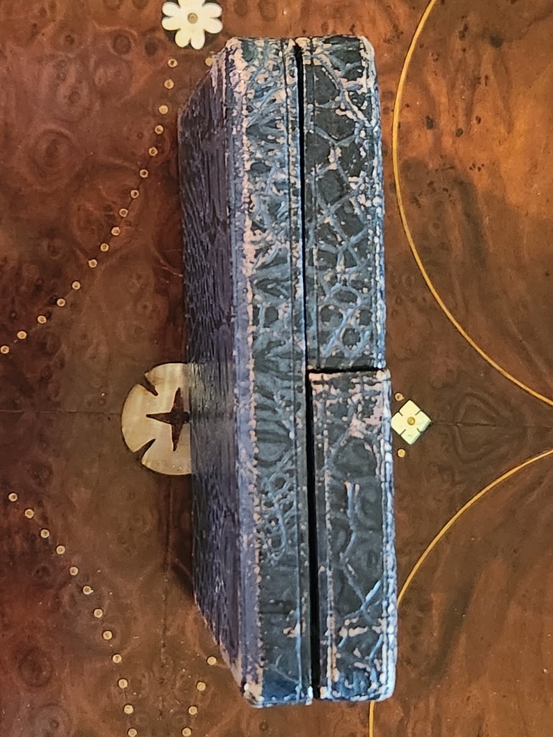 May include: A dark blue, rectangular box with a textured, patterned surface. The box is closed and has a hinge on one side.