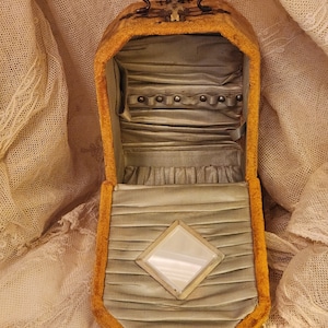 May include: A vintage jewelry box with a hinged lid and a small mirror inside. The box is made of a yellow fabric with a velvet-like texture. The inside of the box is lined with a light blue fabric and has a row of small metal studs.