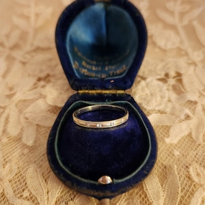 May include: A silver ring with small diamonds set in a blue velvet ring box. The box has a gold trim and the words "Presented for" and "Pillow-Talk" are visible.