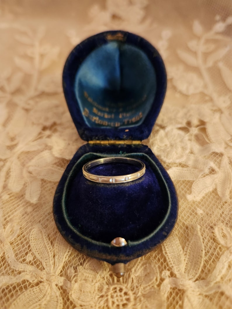 May include: A silver ring with small diamonds set in a blue velvet ring box. The box has a gold trim and the words "Presented for" and "Pillow-Talk" are visible.