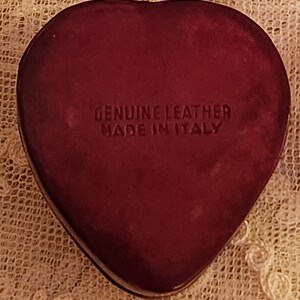 May include: A heart-shaped, burgundy leather box with the text "GENUINE LEATHER MADE IN ITALY" embossed on the front.