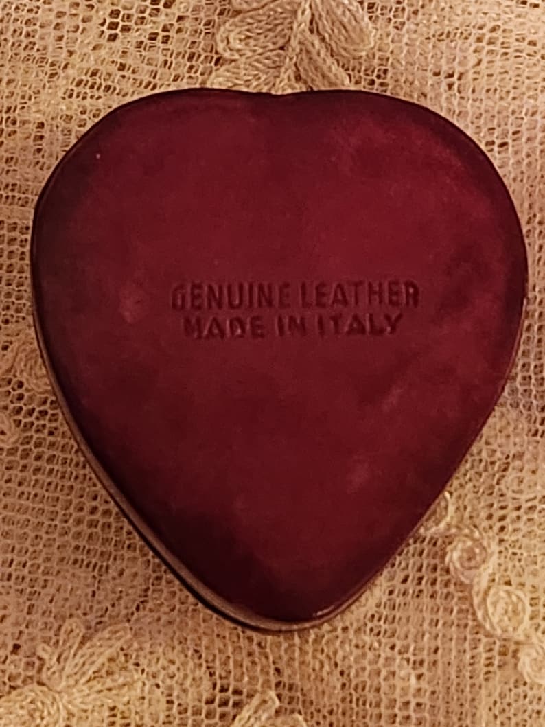 May include: A heart-shaped, burgundy leather box with the text "GENUINE LEATHER MADE IN ITALY" embossed on the front.