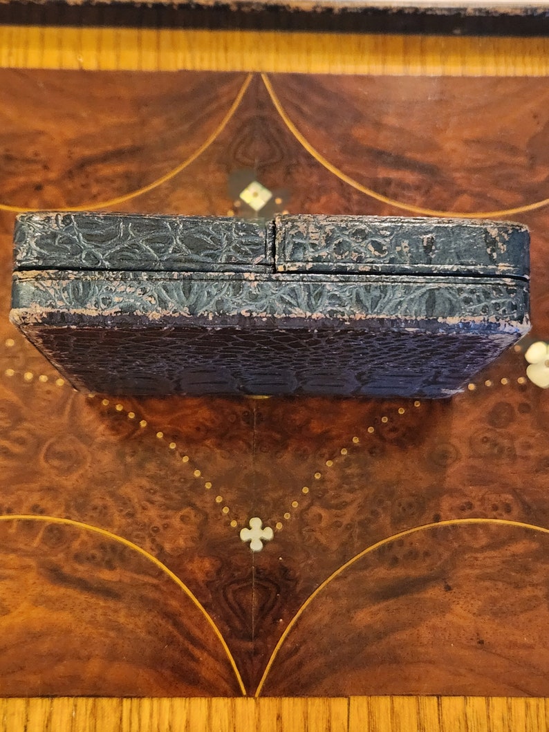 May include: A black leather box with a textured surface. The box is closed and sitting on a wooden surface.