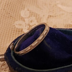May include: A silver wedding band with a textured surface, resting in a blue velvet ring box. The band is inscribed with "14K" on the inside.