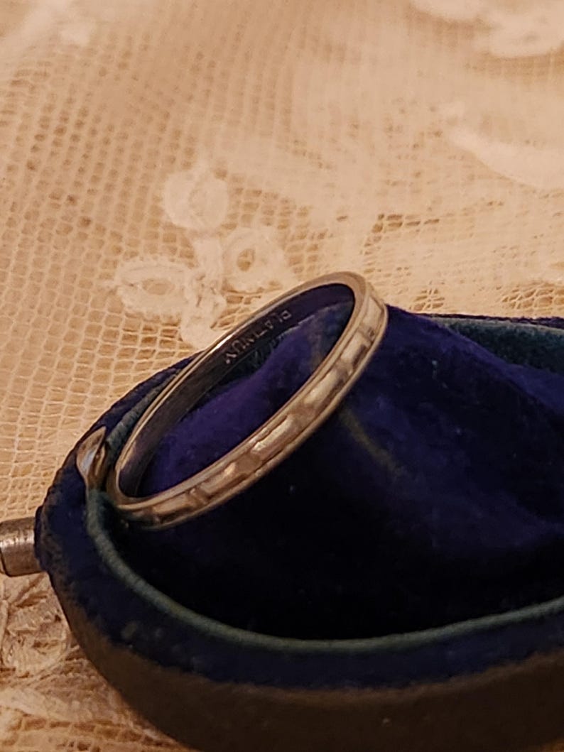May include: A silver wedding band with a textured surface, resting in a blue velvet ring box. The band is inscribed with "14K" on the inside.