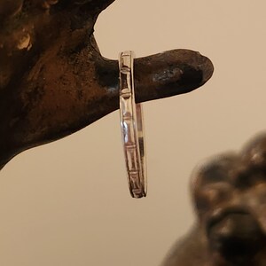 May include: A silver band ring with a textured design. The ring is thin and delicate.
