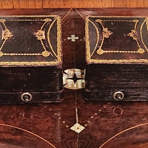 Puede incluir: Dos peque&ntilde;as cajas cuadradas de cuero marr&oacute;n con adornos dorados y dise&ntilde;os ornamentados. Cada caja tiene un peque&ntilde;o pomo plateado en la parte delantera.