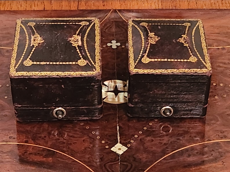 Puede incluir: Dos peque&ntilde;as cajas cuadradas de cuero marr&oacute;n con adornos dorados y dise&ntilde;os ornamentados. Cada caja tiene un peque&ntilde;o pomo plateado en la parte delantera.