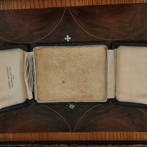 May include: An empty, black, velvet-lined jewelry box with a white satin interior. The box is open and the lid is folded back. The box has a label on the inside that reads "Gimbel Brothers, Philadelphia - New York, Paris".