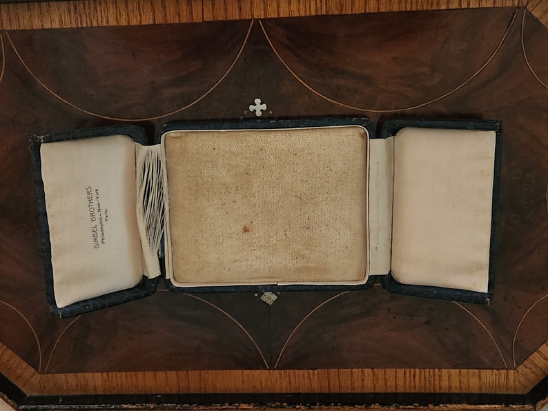 May include: An empty, black, velvet-lined jewelry box with a white satin interior. The box is open and the lid is folded back. The box has a label on the inside that reads "Gimbel Brothers, Philadelphia - New York, Paris".