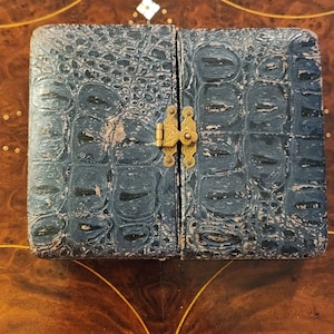 May include: A small, black, leather-bound photo album with a brass clasp. The album has a crocodile-embossed pattern.