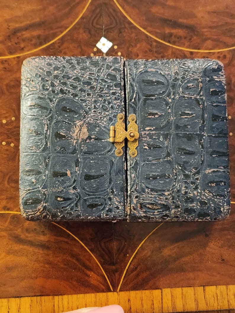 May include: A small, black, leather-bound photo album with a brass clasp. The album has a crocodile-embossed pattern.