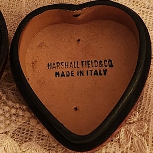 May include: A heart-shaped leather box with a black rim. The inside of the box is brown and has the text "MARSHALL FIELD & CO MADE IN ITALY" printed on it.