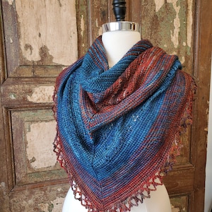 May include: A blue and red knitted shawl with a crocheted border. The shawl is draped over a white mannequin.