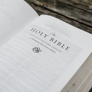 Puede incluir: Primer plano de una Biblia abierta con el t&iacute;tulo "The Holy Bible, English Standard Version, Containing the Old and New Testaments" impreso en la p&aacute;gina. El logotipo de ESV es visible debajo del t&iacute;tulo.